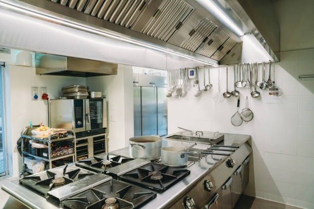 Commercial kitchen with stainless steel appliances, range, pots, oven, and hanging utensils.