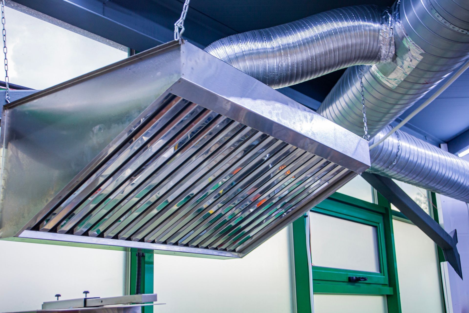 Stainless steel range hood with ventilation ductwork in a commercial kitchen setting.