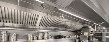 Stainless steel commercial kitchen hood with cooking utensils.