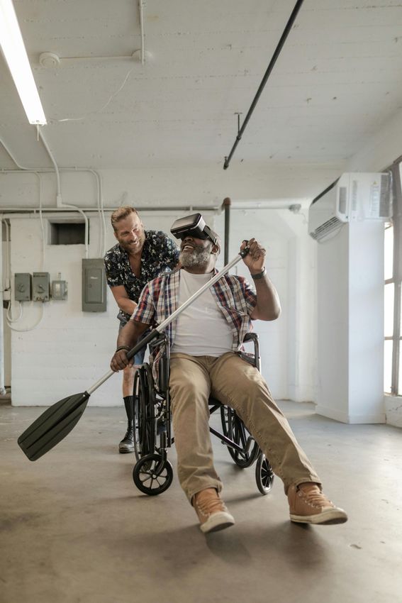 Man in wheelchair pretending to row, with a person pushing him indoors.