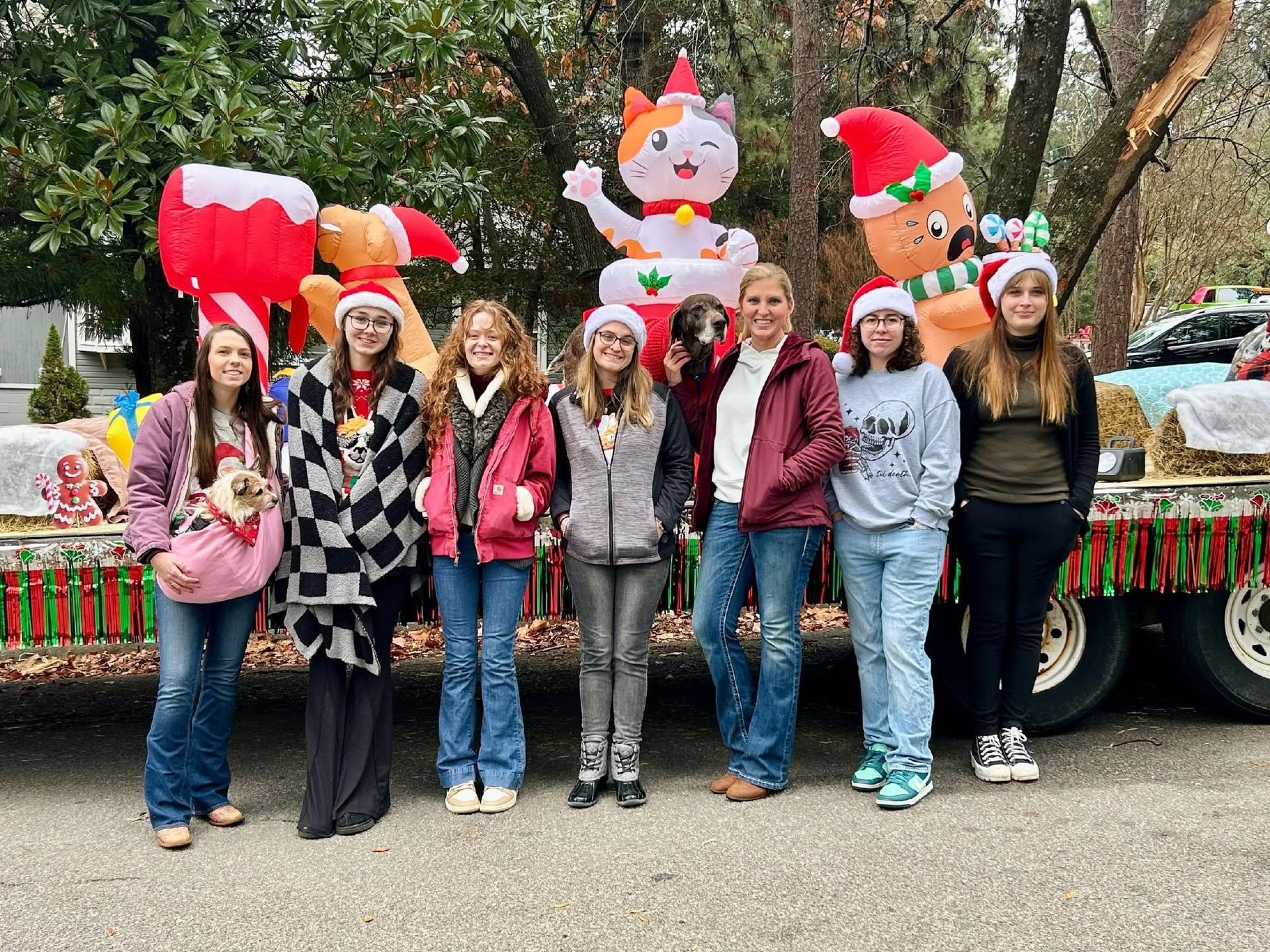 Group posing by a decorated holiday float with a candy cane, Santa, and a snowman inflatable.