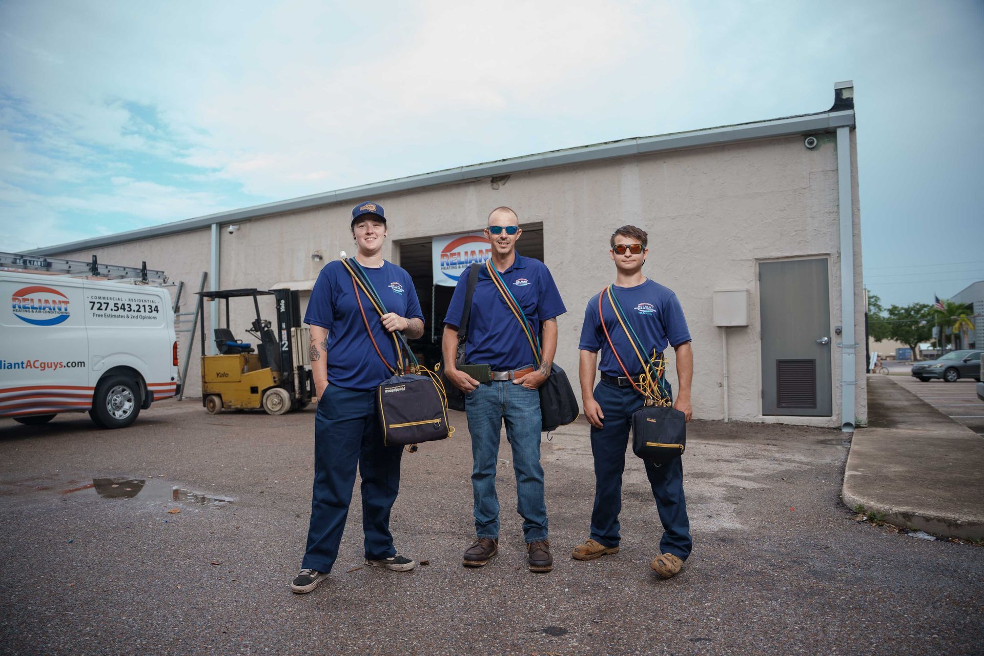 Three Reliant Heating & Air Conditioning technician are standing in front of a building.