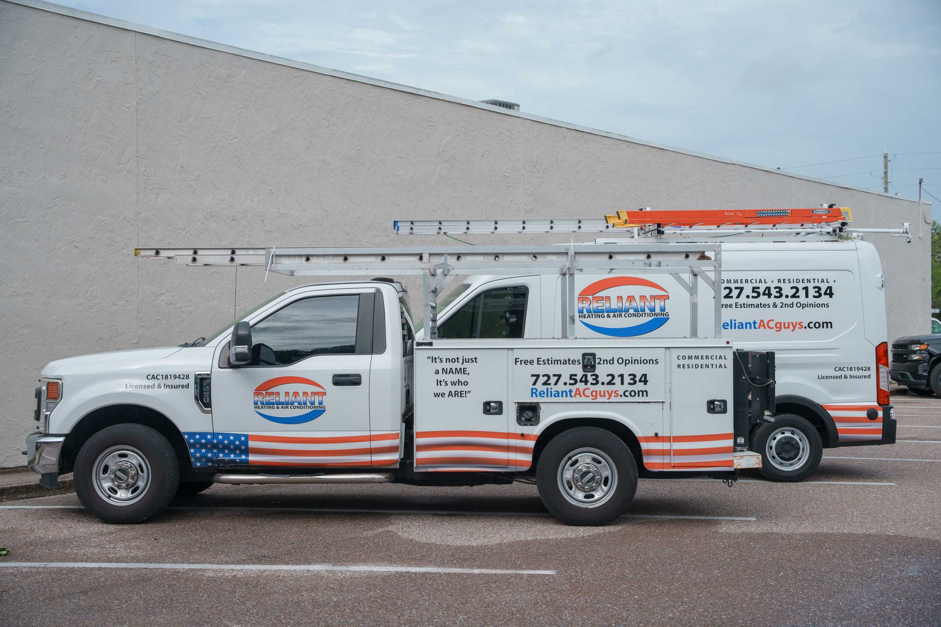 A Reliant Heating & Air Conditioning truck with an American flag on the side is parked in front of a building.