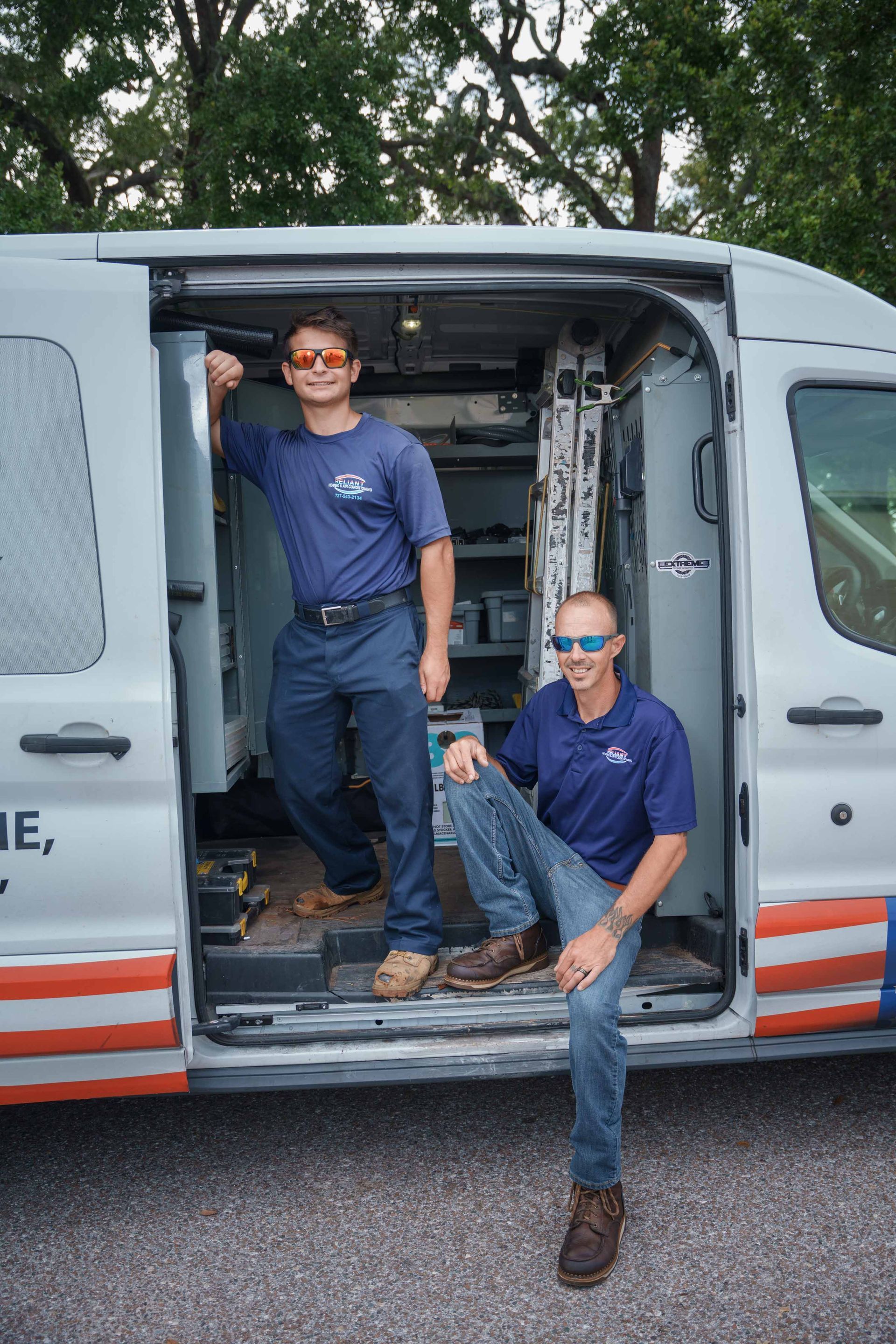 Two Reliant Heating & Air Conditioning technician are standing in the doorway of a van.