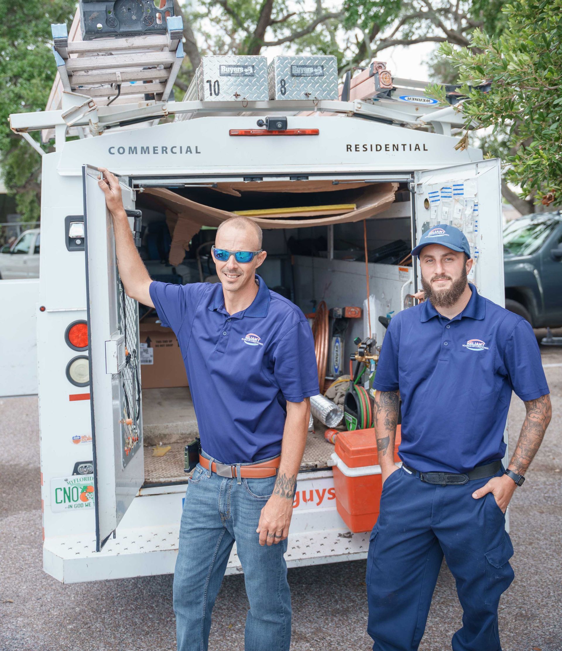 Two Reliant Heating & Air Conditioning technician in blue shirts are standing in front of a utility truck.