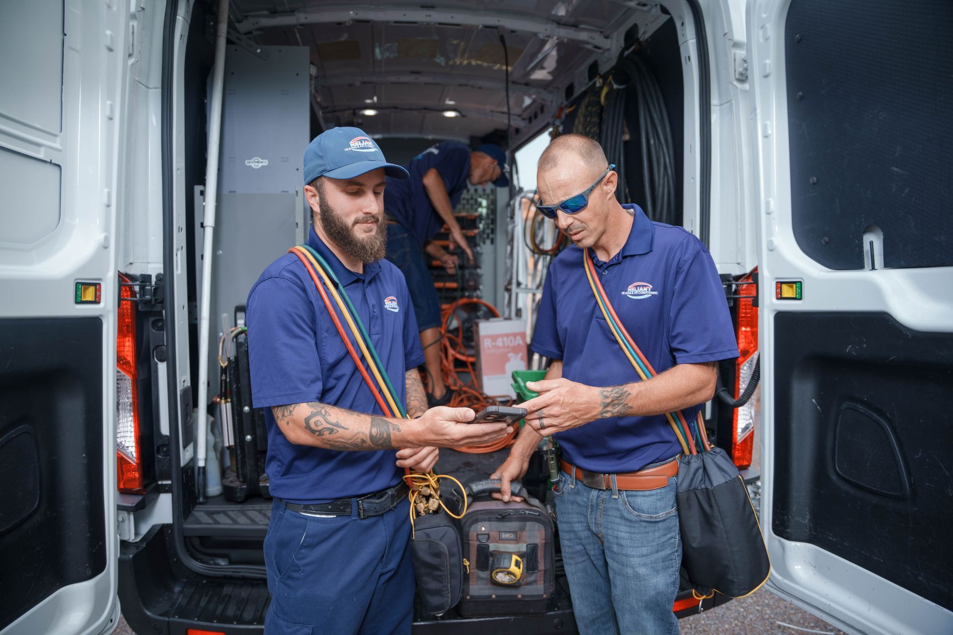 Two Reliant Heating & Air Conditioning technician are standing next to each other in front of a van.