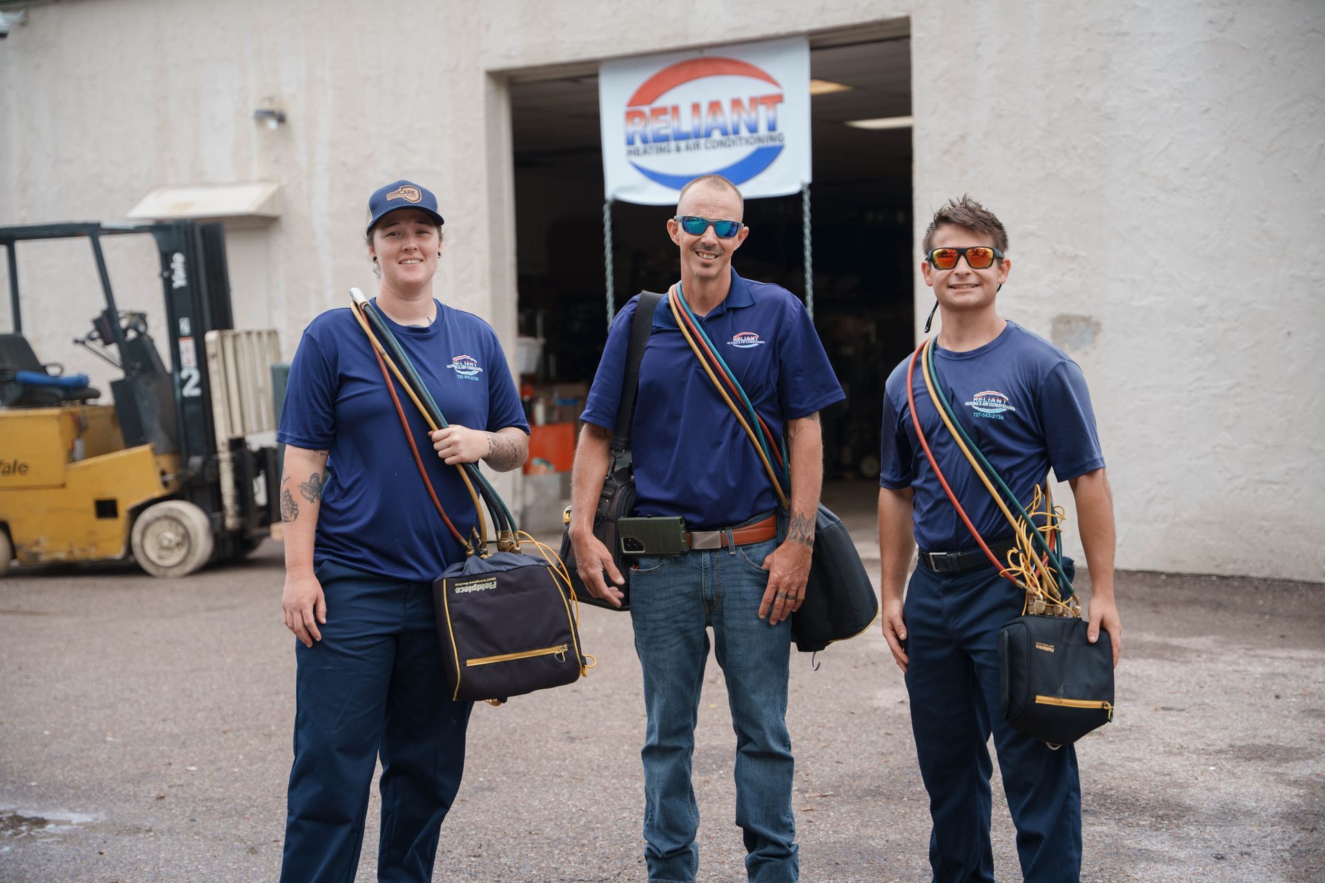 Three Reliant Heating & Air Conditioning technician are standing in front of a building with a forklift in the background.