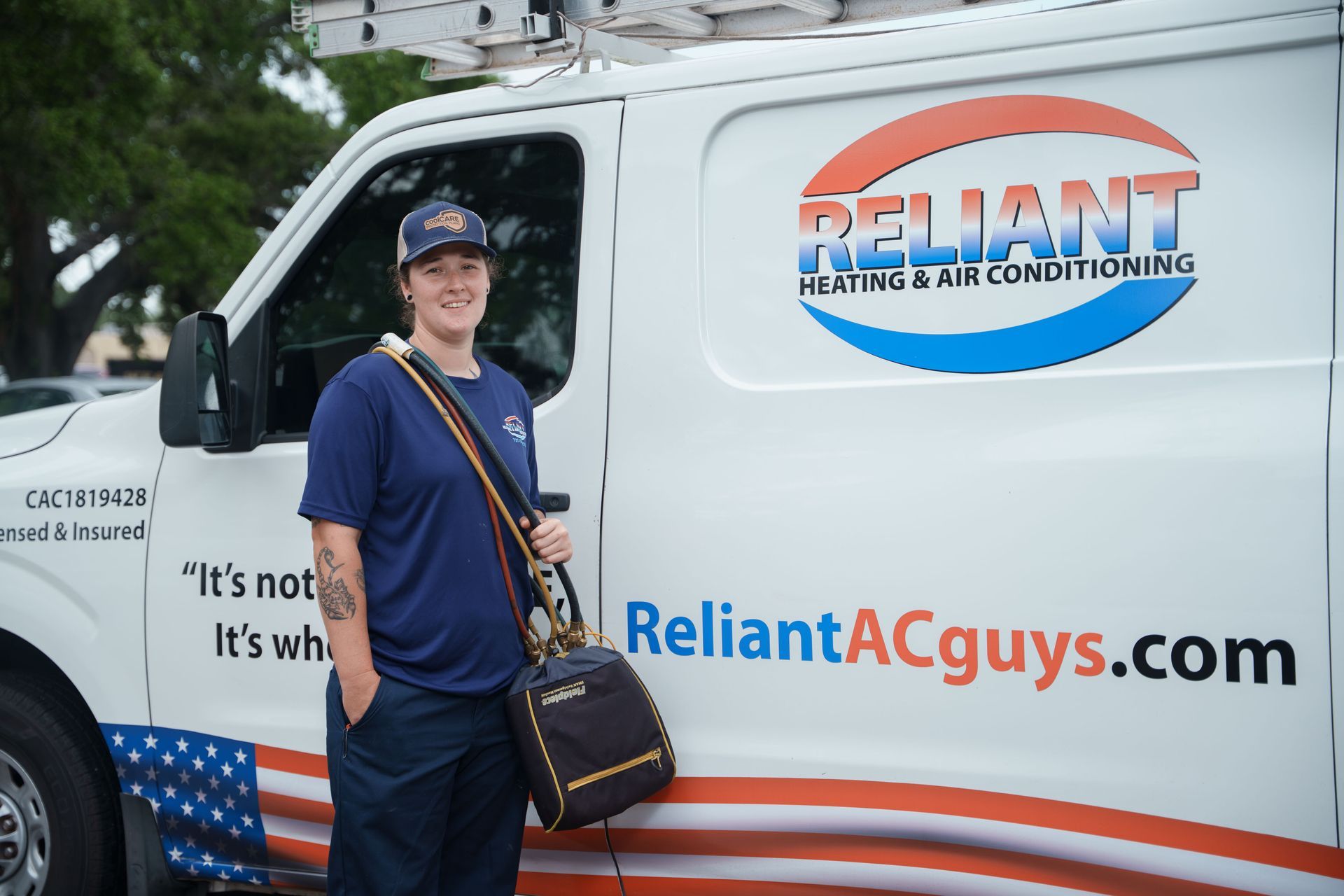 A Reliant Heating & Air Conditioning technician is standing in front of a reliant heating and air conditioning van.