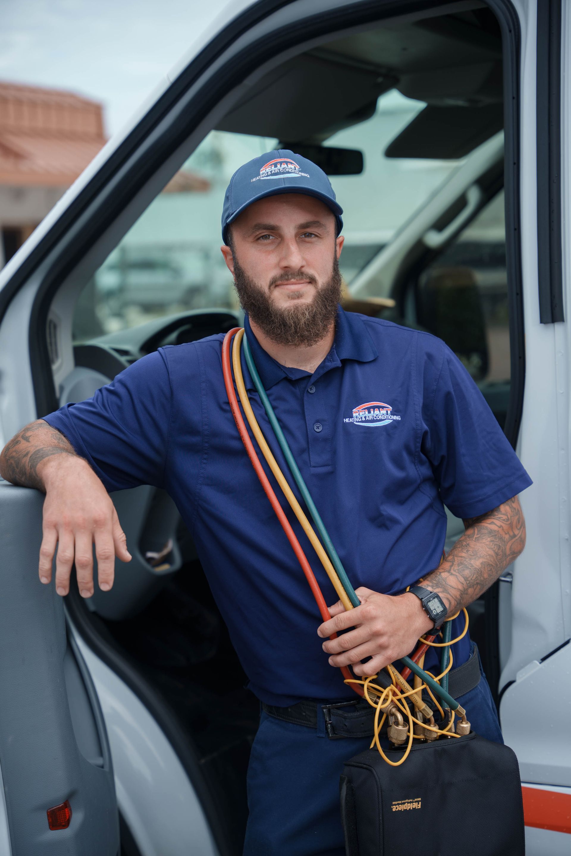 A Reliant Heating & Air Conditioning technician with a beard is leaning on the door of a van.