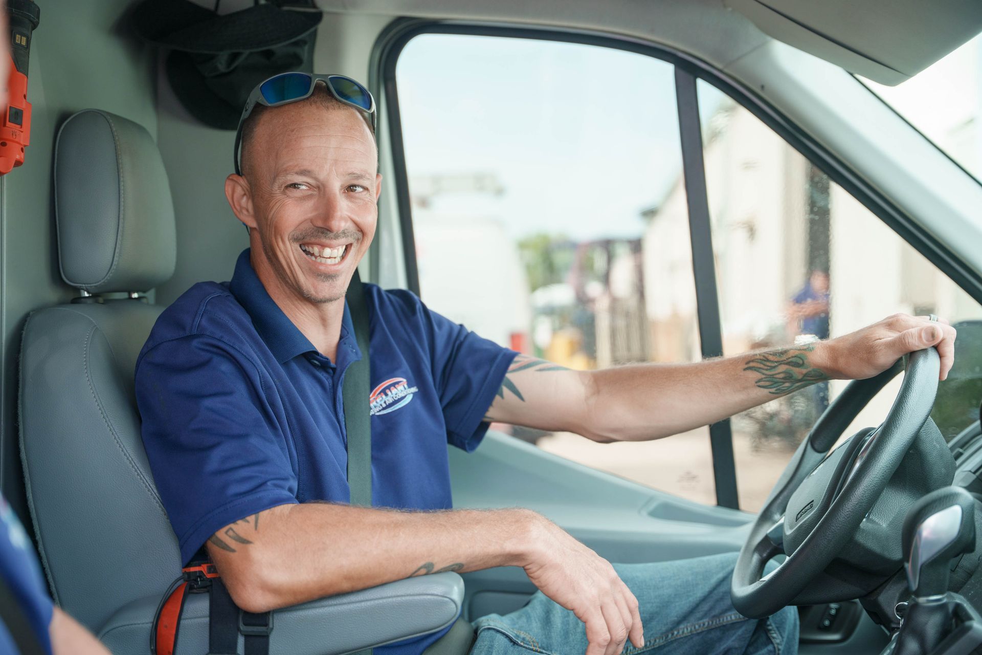 A Reliant Heating & Air Conditioning technician is sitting in the driver 's seat of a van and smiling.