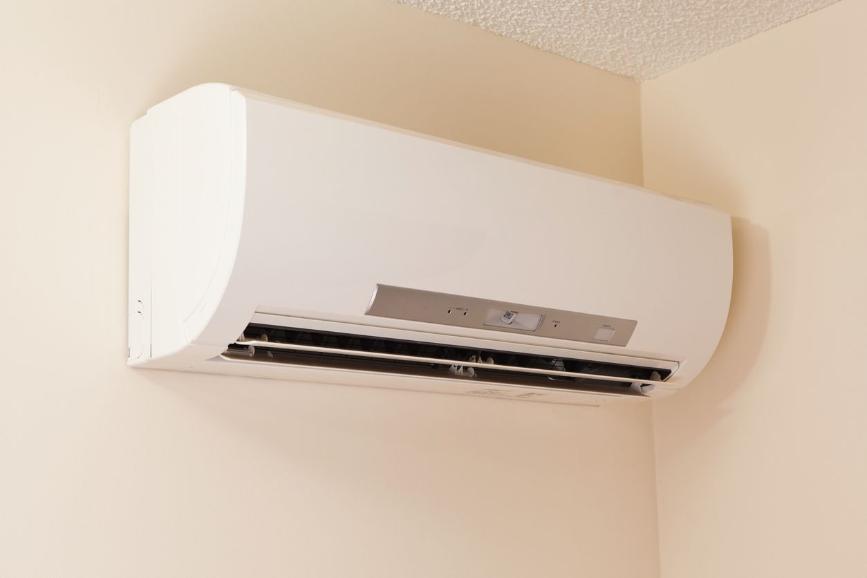A white air conditioner is hanging on a wall in a room Installed by Reliant Heating & Air Conditioning.