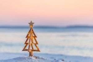 A small wooden christmas tree is sitting on top of a snow covered beach.