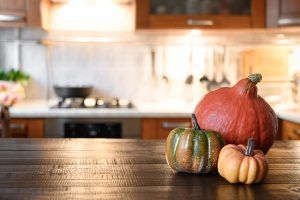 Three pumpkins are sitting on a wooden table in a kitchen.