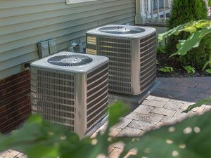 Two air conditioners are sitting on the side of a house Installed by Reliant Heating & Air Conditioning.