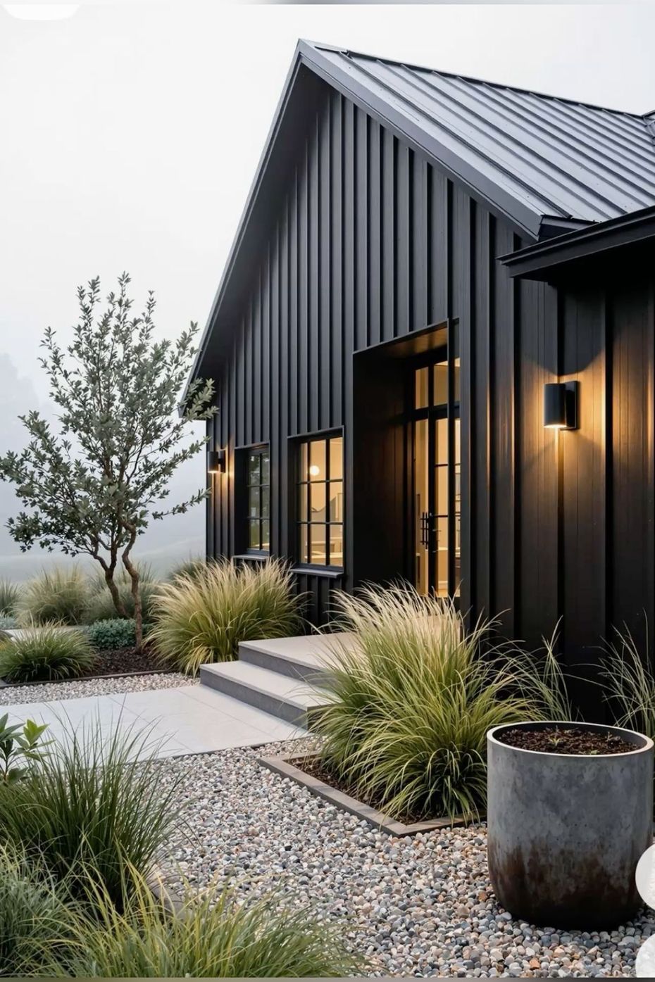 Black modern house with metal roof, steps, gravel path, and lush landscaping.
