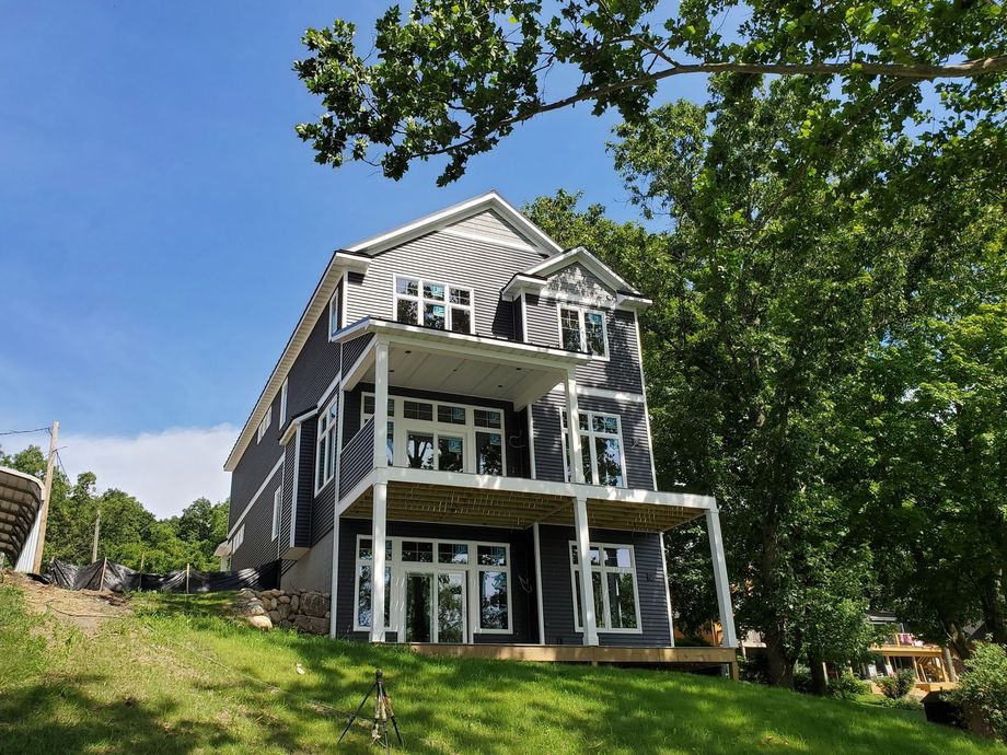 Three-story house with dark gray siding and white trim on a grassy hill with large windows, blue sky.