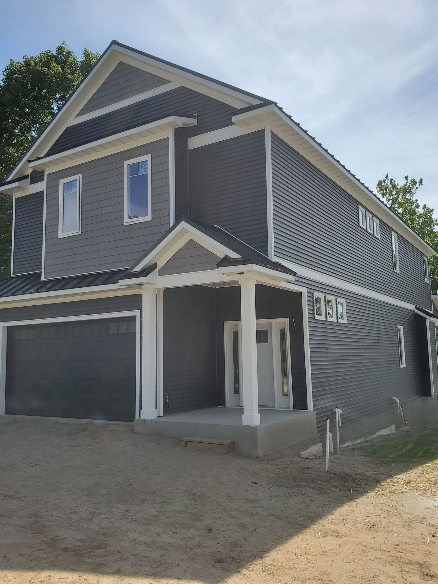 Two-story gray house with white trim; garage, entrance with pillars, windows, gravel yard.