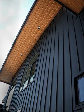Dark gray house exterior with wooden soffit, windows, and upward angle.