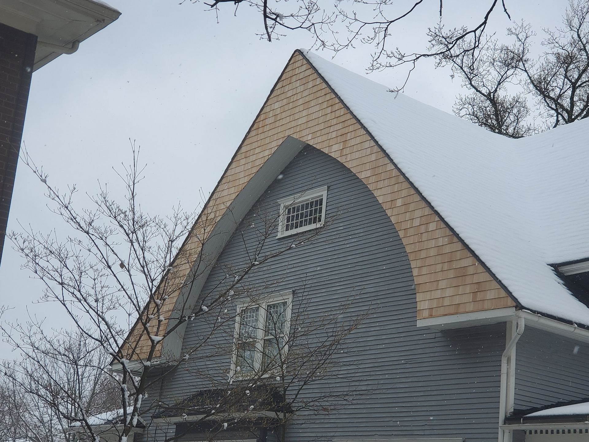 Snowy house gable with curved roof edge, blue siding, and small window.