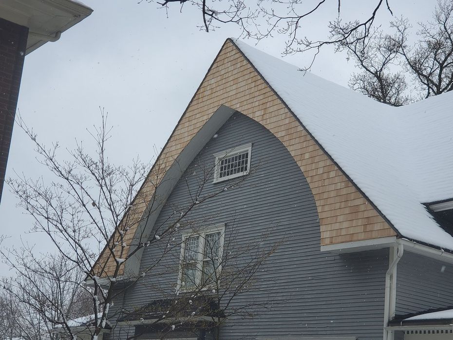 Snowy house gable with curved roof edge, blue siding, and small window.