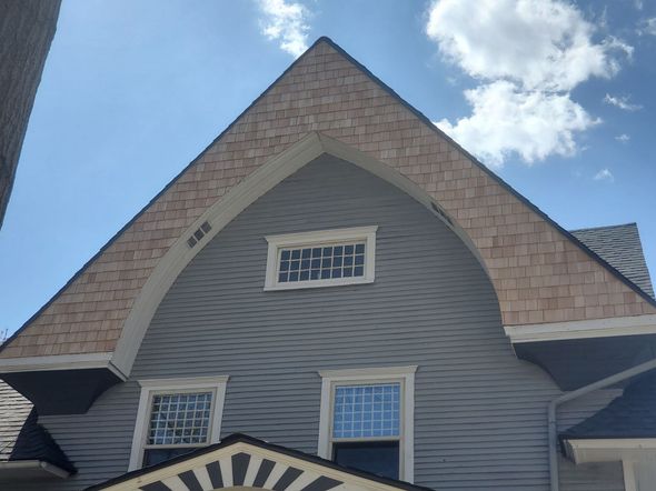Gray house with a wood-shingled gable, white-framed windows, and blue sky.