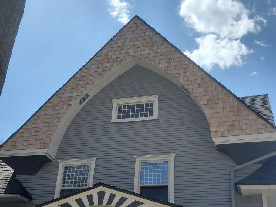 Grey house with arched roofline, cedar shingles, windows, and blue sky.