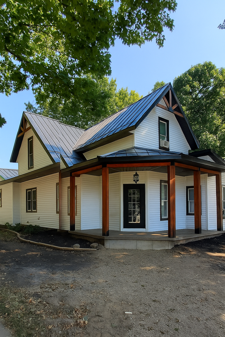 A white farmhouse with a black roof and a wraparound porch with brown supports.