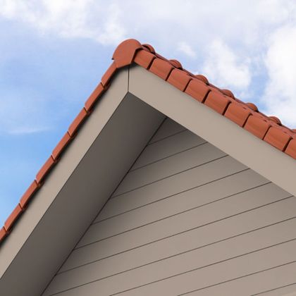 Corner of a roof with red tiles and beige siding against a blue sky.