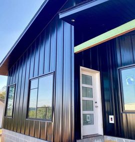 Black modern house with vertical metal siding, white door, and large windows.