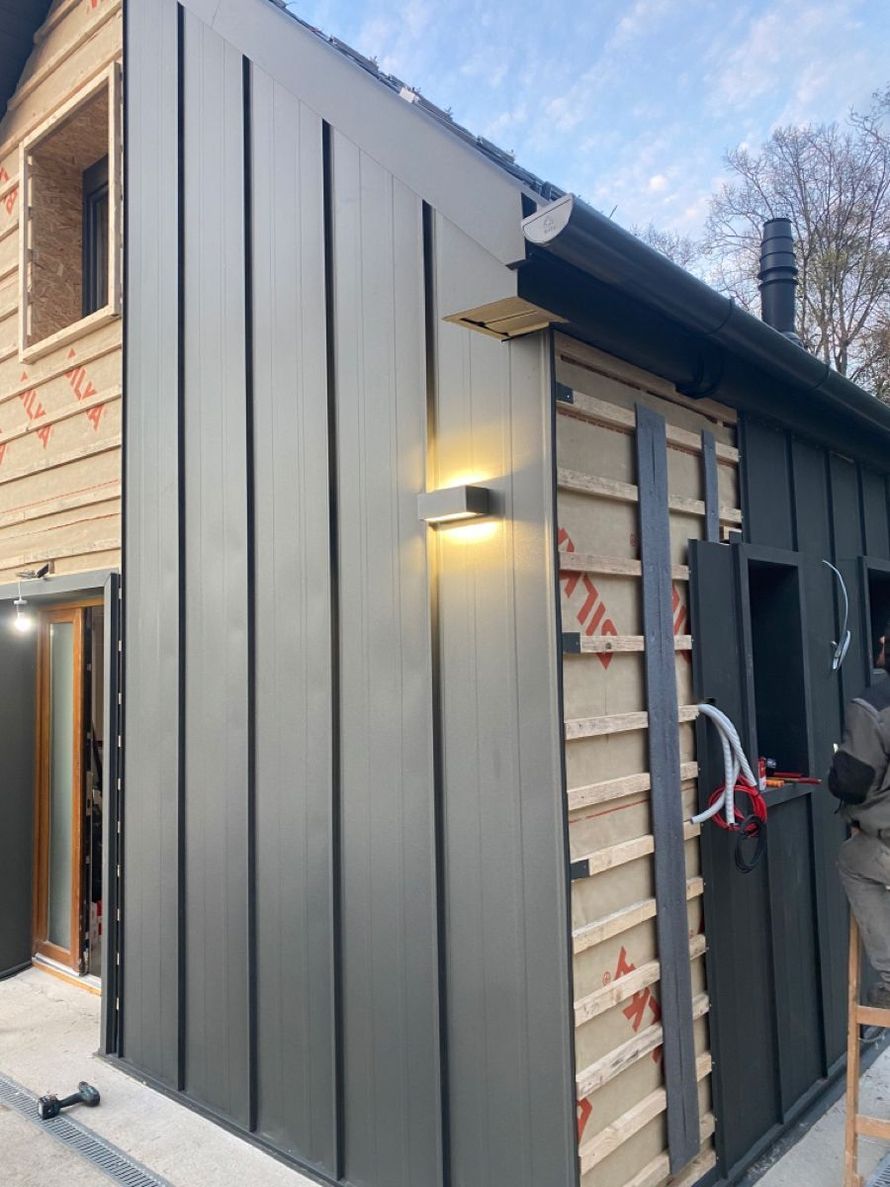 Exterior of a building under construction with gray siding. Light fixture installed, exposed wooden framing.