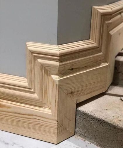 Wooden crown molding installed at a corner of a gray wall and white marble floor.