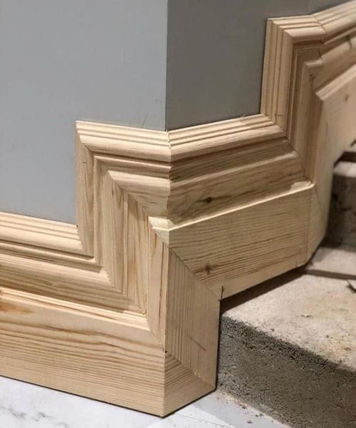 Wooden molding corner, with intricate cuts, meeting at a wall corner. Light wood, gray wall.