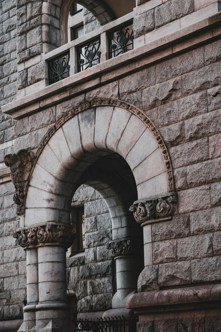 Stone archway entrance to a building with ornate details and a balcony above.