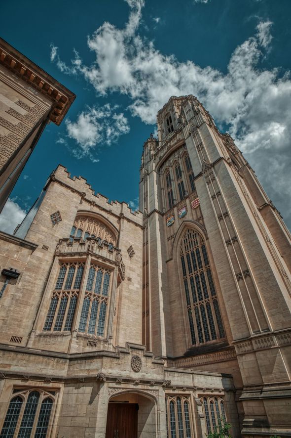 Stone Gothic building with tall tower under a cloudy blue sky.