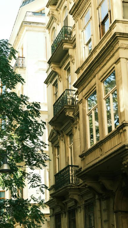 Ornate beige building facade with balconies and windows, trees in the foreground.