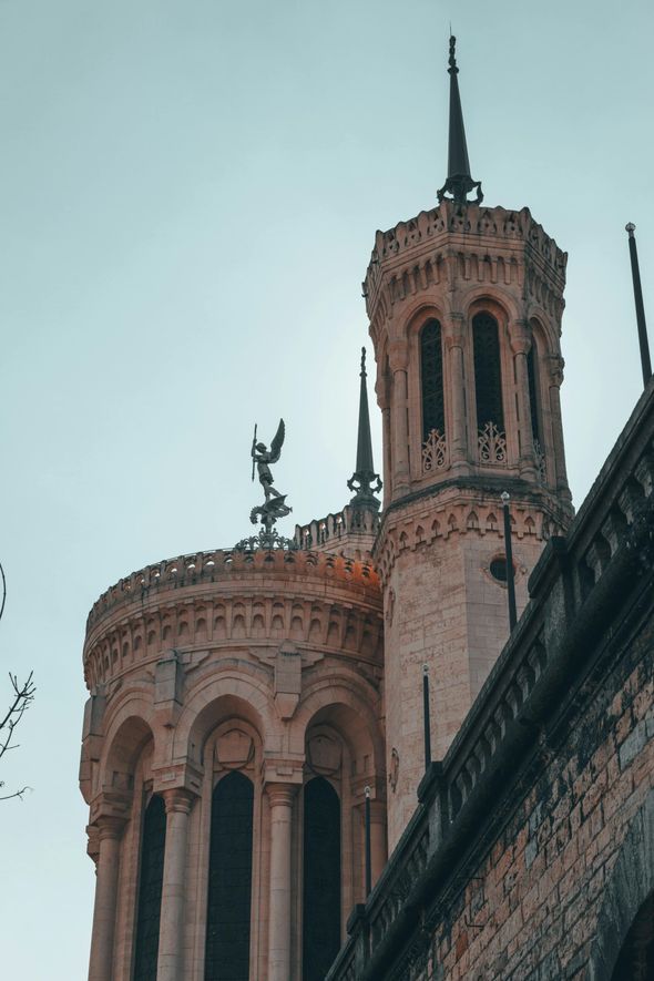 Beige basilica towers against a light blue sky; statue on top.