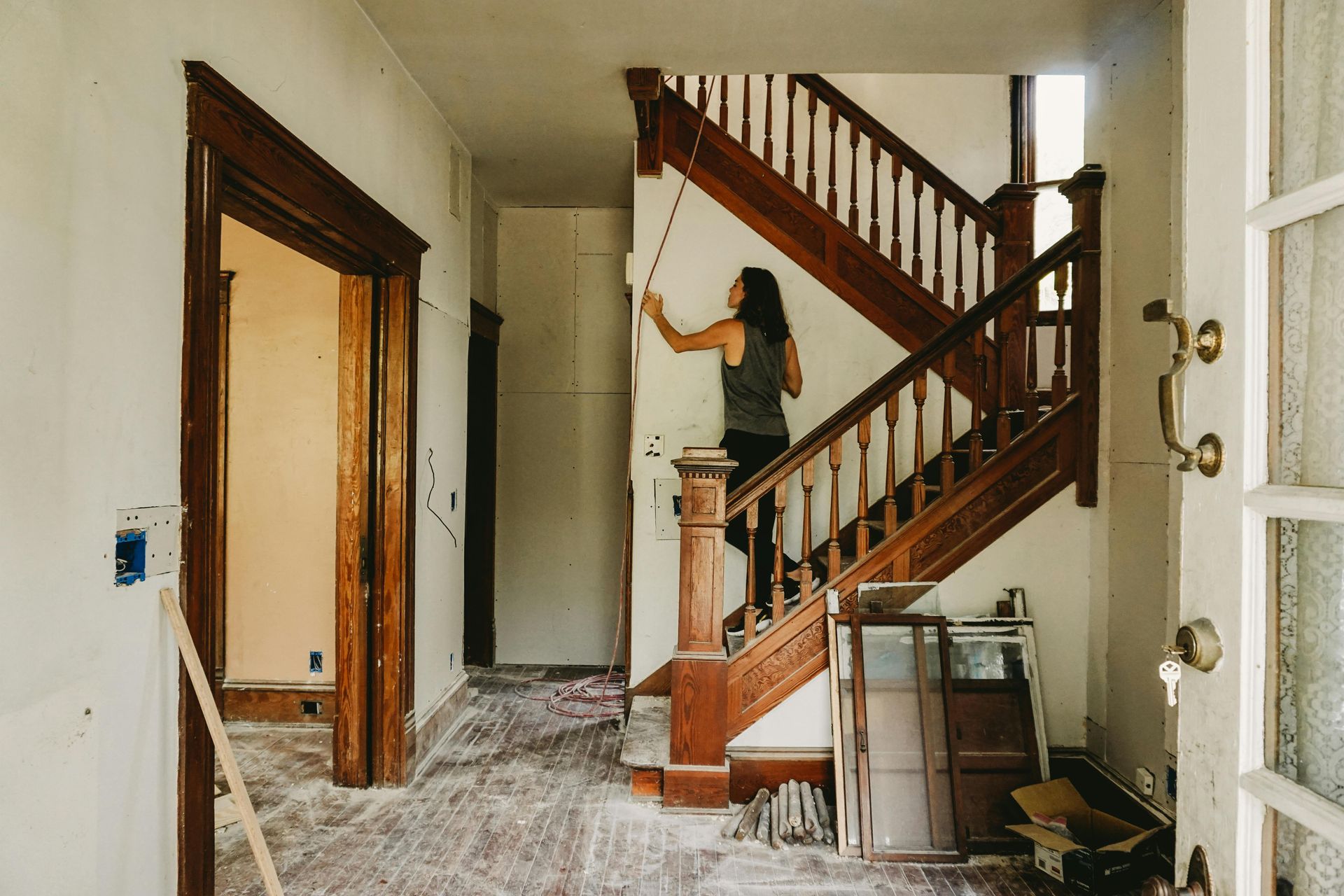Person painting a wall near a wooden staircase in a room under renovation.
