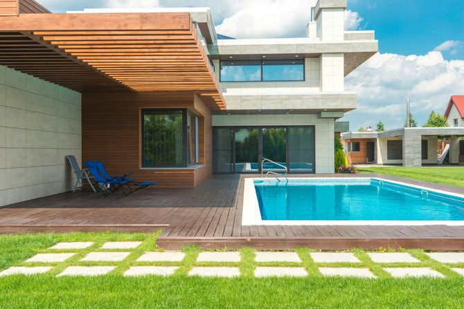 Modern house with a swimming pool and wooden deck on a sunny day.