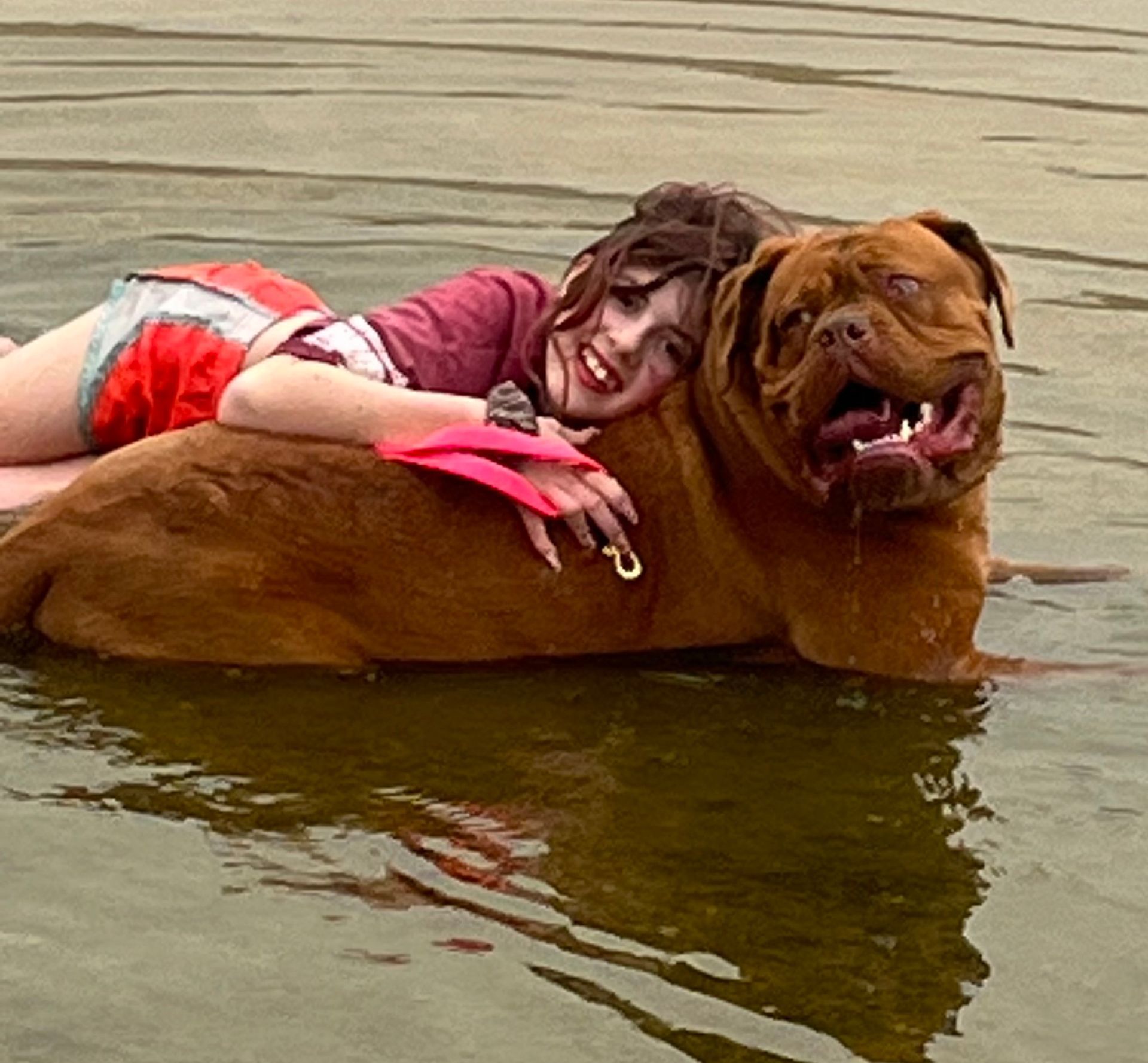 A woman is laying on top of a brown dog in the water