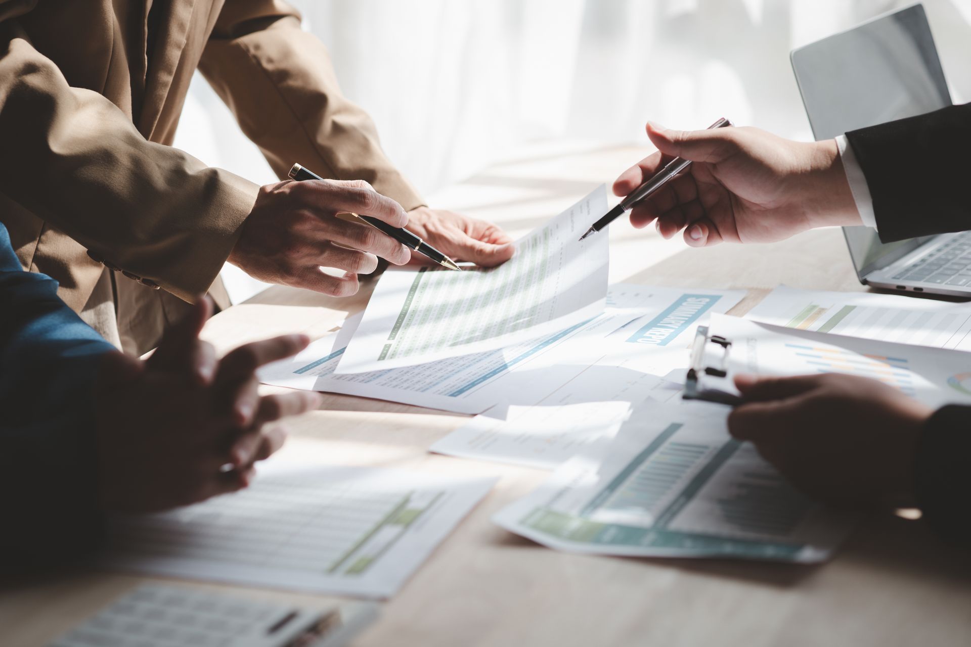 People in a business meeting reviewing documents, using pens to point and discuss.