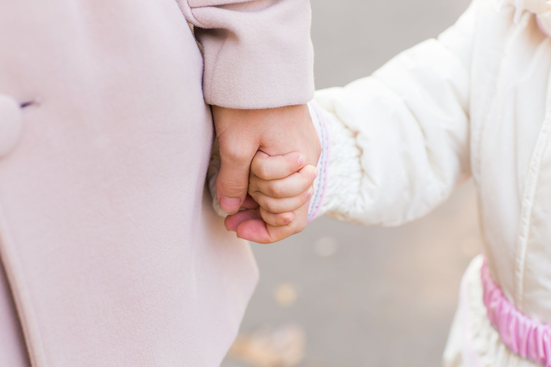 Adult and child holding hands; soft lighting, light colors.