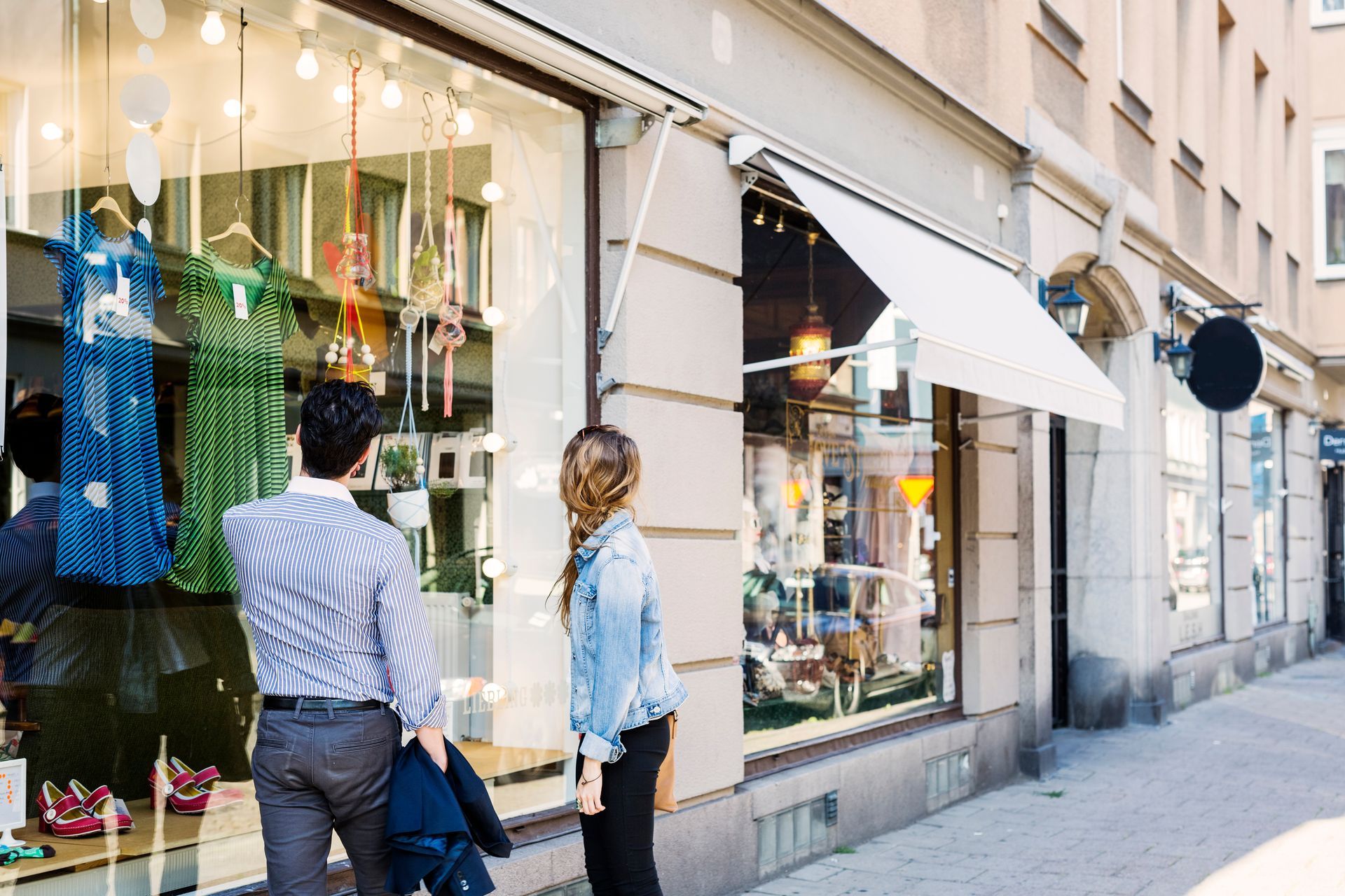 Couple looking at the window display of a boutique store on a sunny day.