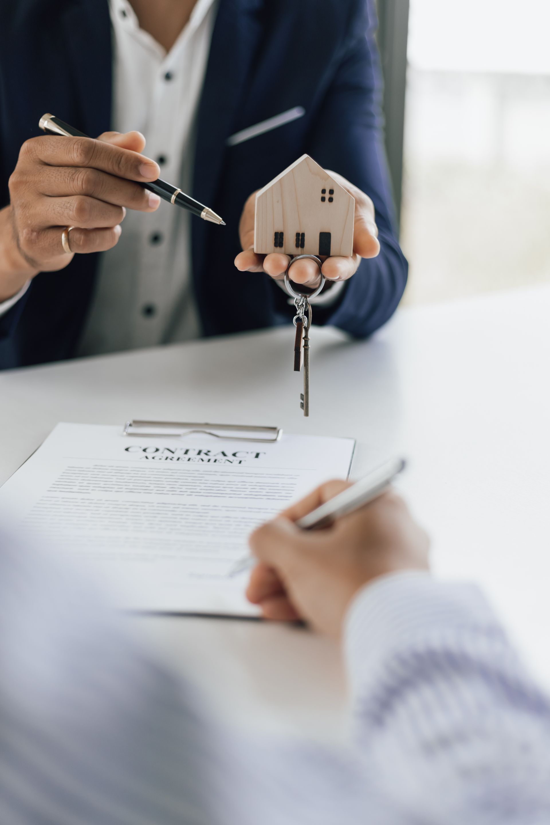 Real estate agent pointing at a house model above a signed contract.