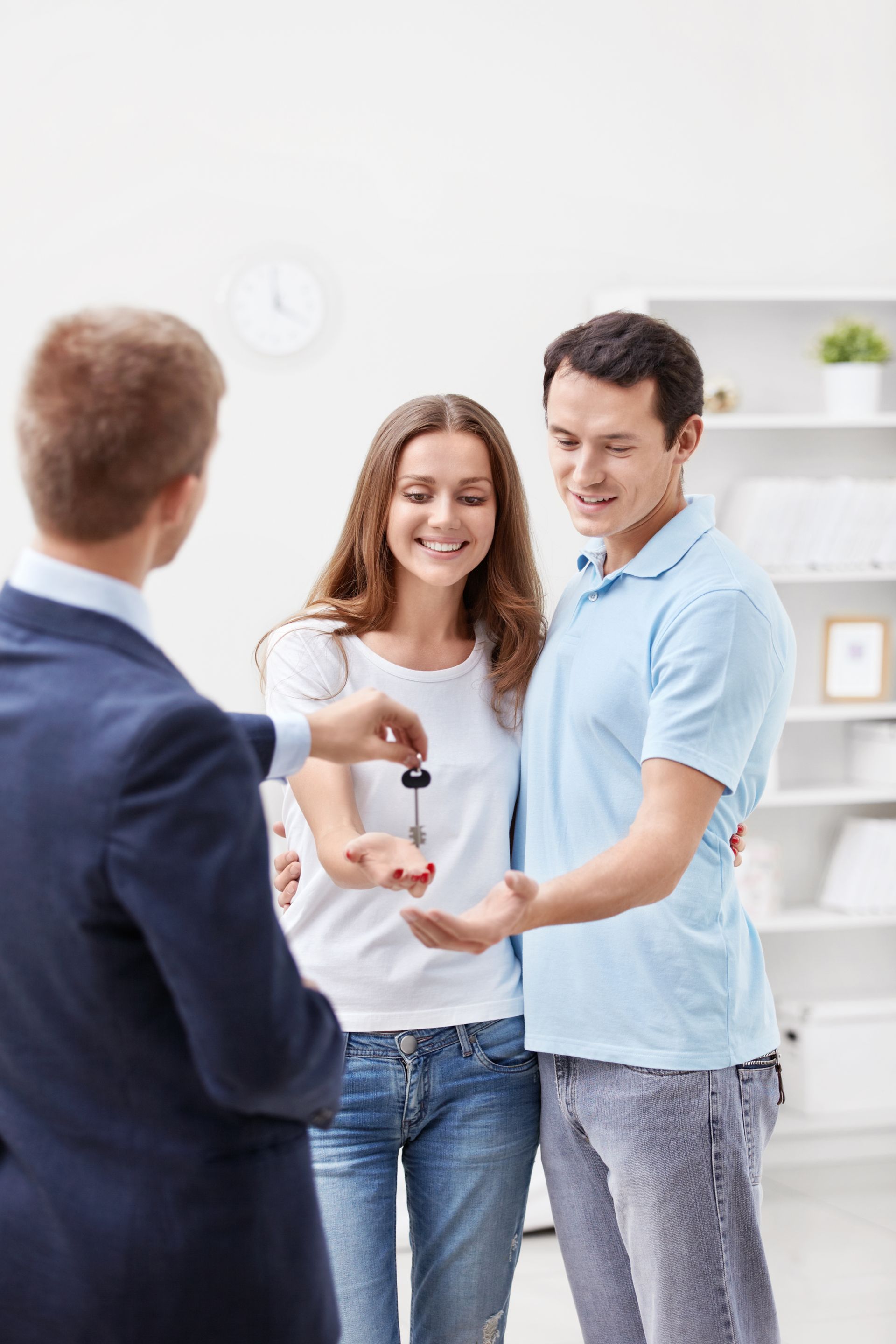 Real estate agent handing keys to smiling couple in a bright, modern room.