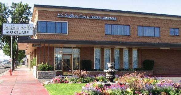 Brick office building with sign, red sidewalk, and flower beds in front