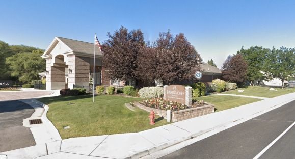 Suburban apartment entrance with landscaped lawn, brick sign, and sidewalk beside a road under blue sky