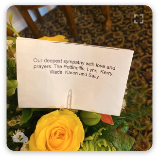 Sympathy note among yellow roses reading, “Our deepest sympathy with love and prayers.”