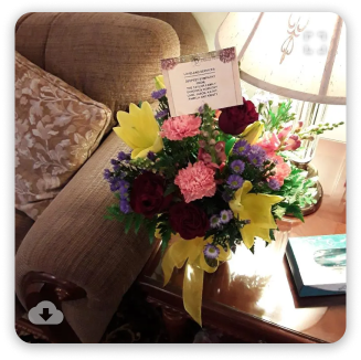 Bouquet of pink, purple, and yellow flowers on a table beside a beige armchair near a sunlit window