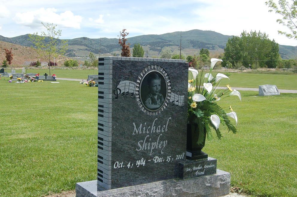 Gravestone with a black headstone and white flowers in a grassy cemetery, mountains in the background