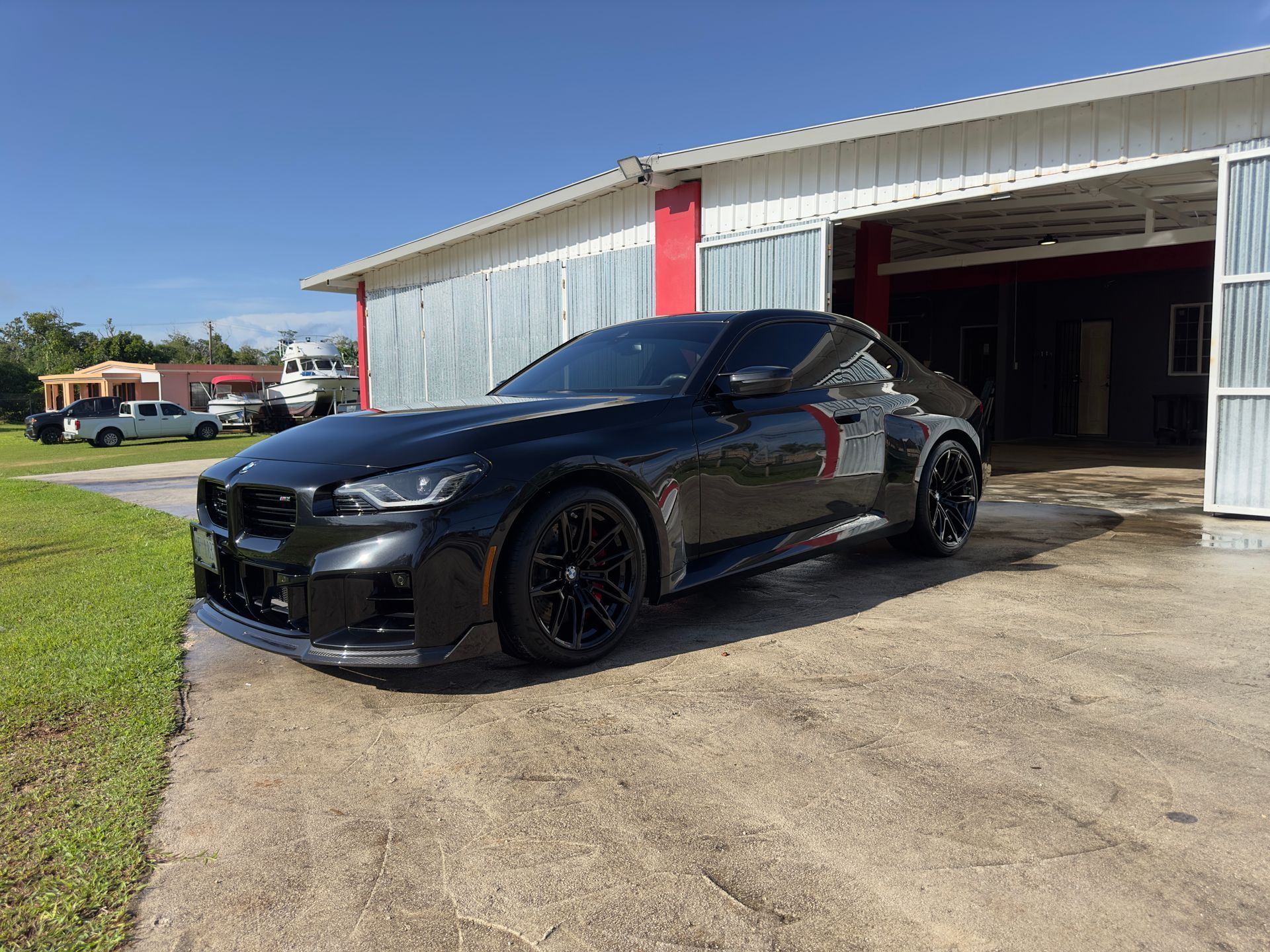 A black BMW coupe parked on a concrete lot in front of a metal-sided building on a sunny day.